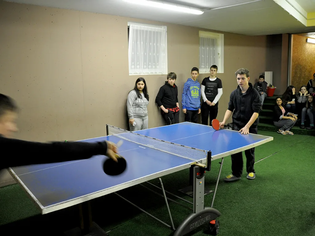 Zwei Jugendliche spielen Tischtennis, andere warten am Rand.
